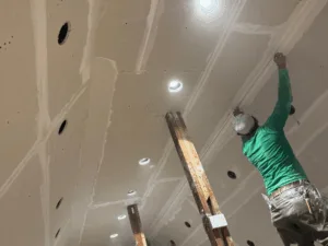Workers performing drywall ceiling finishing with joint compound.