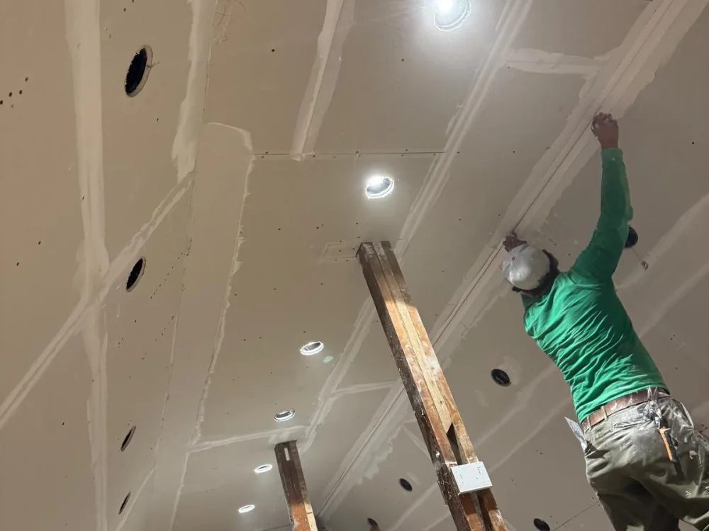 Workers performing drywall ceiling finishing with joint compound.